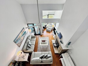 A spacious loft-style living area with a high ceiling, a central seating area, a fireplace, and a view of the outdoors.