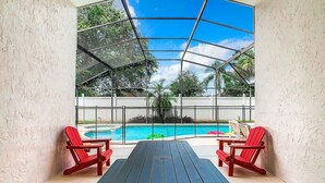 Eine überdachte Terrasse mit Pool, roten Stühlen und einem Tisch.