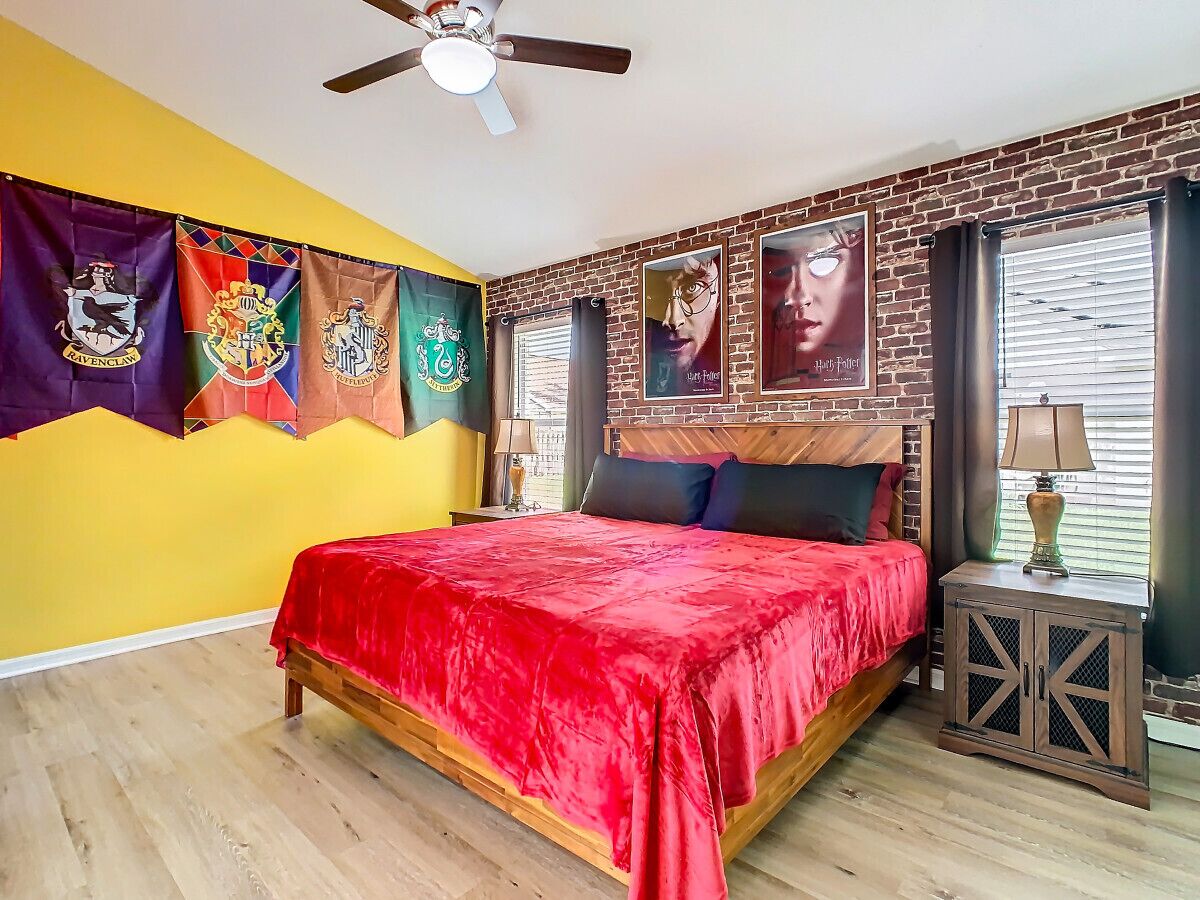 Een slaapkamer met een houten bed, een rode sprei, een plafondventilator en een bakstenen muur.