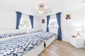 A room with two beds, a ceiling fan, a nightstand with a lamp, and a picture on the wall.