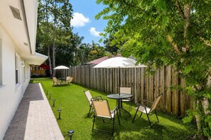 A backyard with a paved walkway, a wooden fence, and outdoor furniture including a table and chairs.