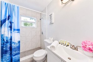 A bathroom with a shower curtain, toilet, sink, and a sign with bathroom rules.