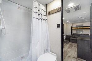 A compact bathroom with a shower, toilet, and a small seating area with a bench and a table. - Coleman Camper Oasis-Beaches-shopping-dining (Pensacola)