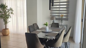 Un comedor moderno con una mesa de vidrio, sillas tapizadas grises, una planta en maceta y una ventana con persianas.
