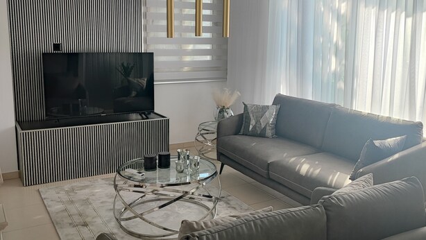 Una sala de estar moderna con un sofá gris, una mesa de centro de vidrio, un televisor de pantalla plana y un mueble de pared a rayas blanco y negro.