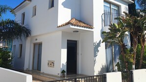 Una casa blanca de dos pisos con techo de tejas, un balcón y una entrada protegida por una reja.