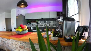 A modern kitchen with a stone accent wall, a fruit bowl, a coffee machine, and a plant in the foreground. - Elegant 70m2 Rooftop at the foot of Le Bourget station (Le Bourget)