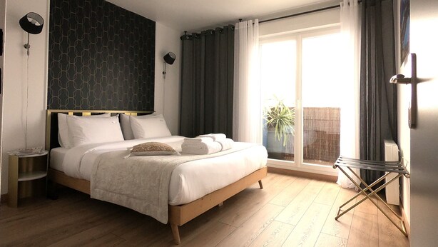 A modern bedroom with a wooden bed, a dark patterned headboard, and a large window with curtains. - Elegant 70m2 Rooftop at the foot of Le Bourget station (Le Bourget)