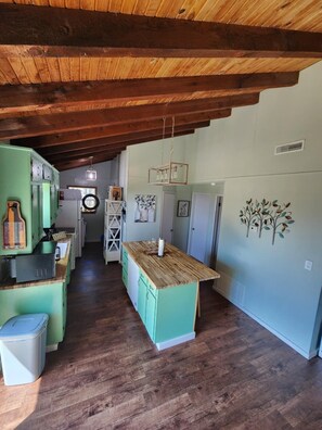 A kitchen with wooden beams, a green island, and a refrigerator.