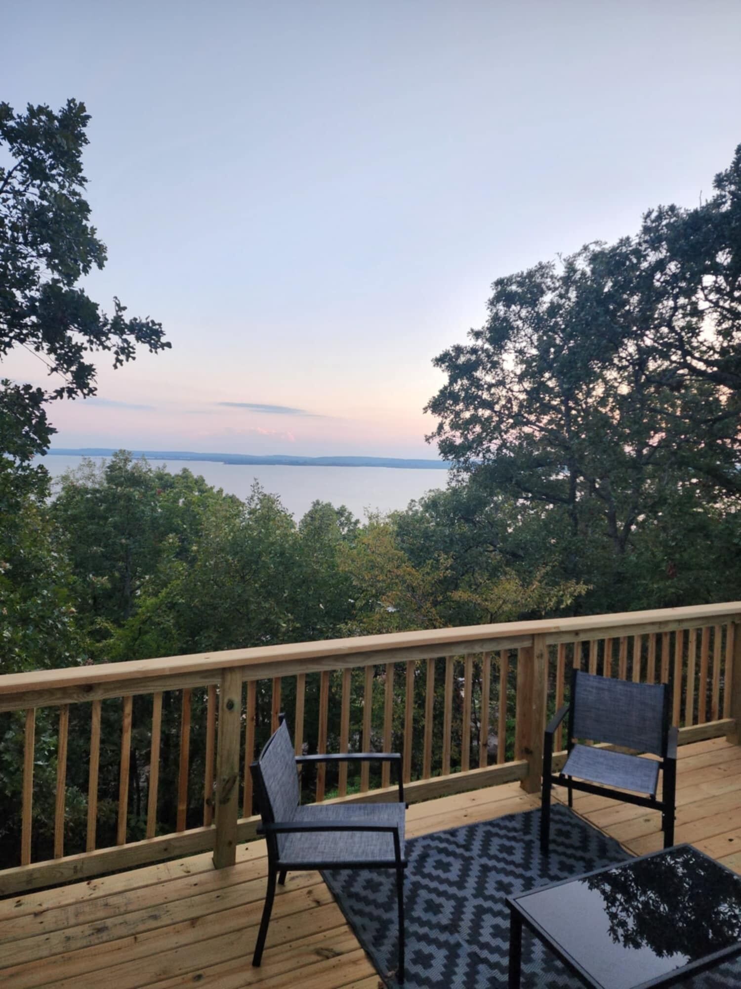 Une terrasse en bois avec deux chaises et une table, donnant sur une étendue d’eau et entourée d’arbres.