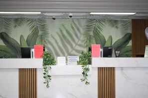A reception desk with a tropical leaf mural, a sign for valued guests, and a security camera.