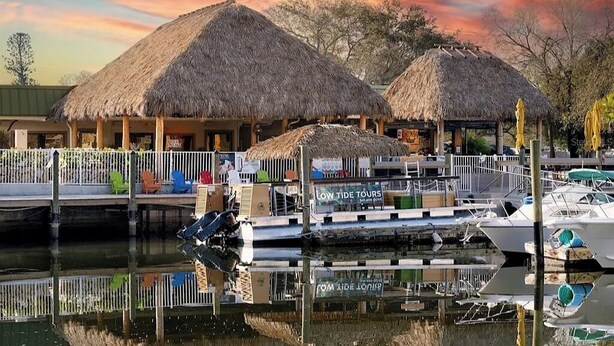 Una zona junto al agua con construcciones de techo de paja, un muelle con barcos y un letrero que dice 'LOW TIDE TOURS'.