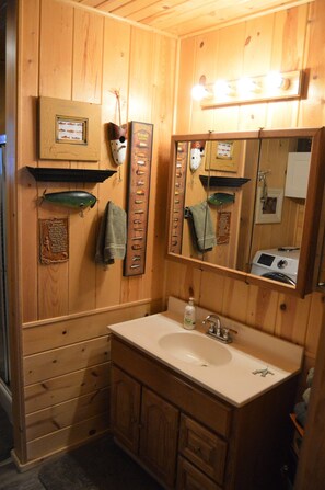 A wooden bathroom with a sink, mirror, towel rack, and a framed fish picture.