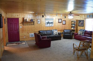 A log cabin interior with a red door, leather sofas, a fireplace, and a 'WELCOME' sign.
