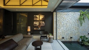 A modern living room with a sofa, a round table, and a chair. There is a stone wall and a water feature in the background.