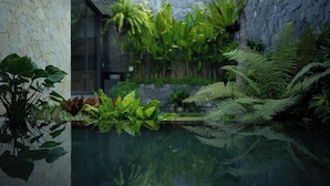 A serene indoor garden with a reflective water feature, lush greenery, and a stone wall.