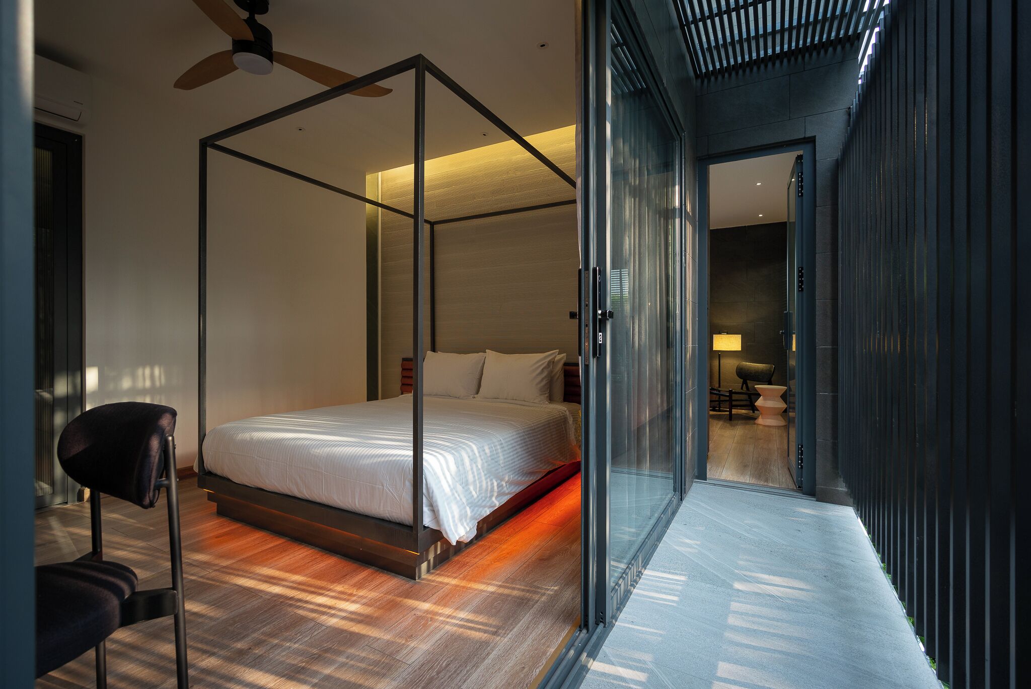 A modern bedroom with a four-poster bed, a glass partition, and a wooden floor.