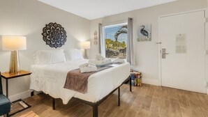 Une chambre d’hôtel avec un lit, une lampe, un élément décoratif mural, une fenêtre donnant sur un paysage agréable et une porte.