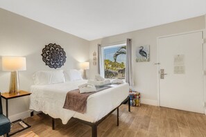 Hotellihuone, jossa on sänky, lamppu, koristeellinen seinäelementti, ikkuna, josta on näkymä, ja ovi.