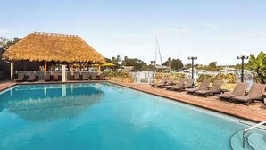 Une piscine avec des chaises longues et une structure dotée d’un toit de chaume.