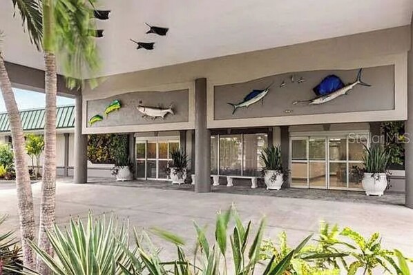 A modern building with a glass facade, palm trees, and decorative fish sculptures on the exterior wall.
