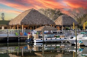 A waterfront area with thatched-roof structures, a dock with boats, and a sign for 'LOW TIDE TOURS'.