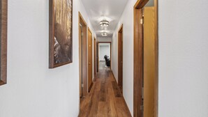 A hallway with wooden floors and white walls, featuring framed artwork and wooden doors. - Country Club (Flagstaff)