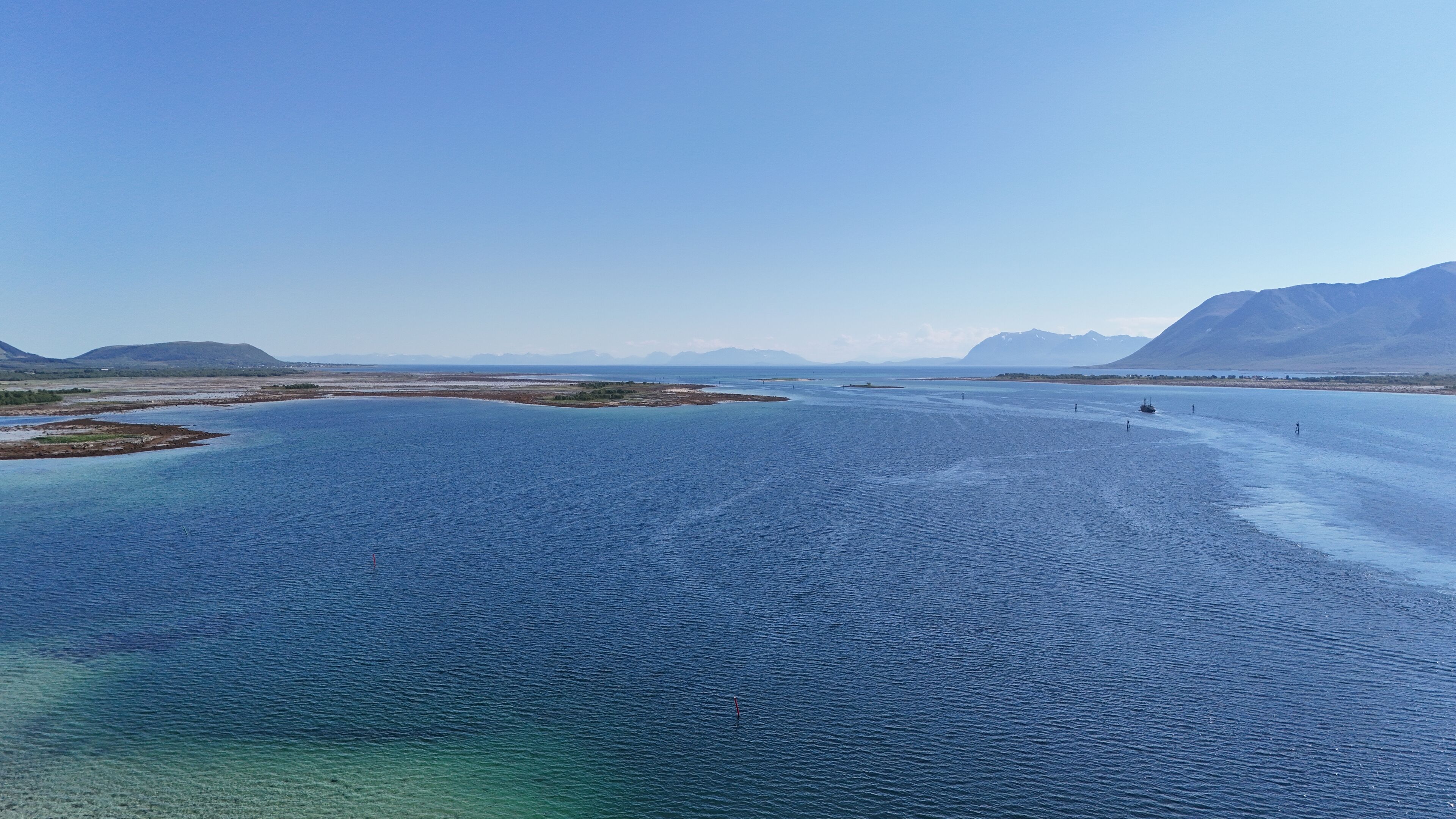 Een uitgestrekte waterpartij met helderblauw water, omringd door land en bergen op de achtergrond.