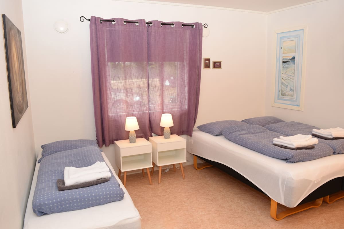 A room with two beds, each with a pillow and a folded towel. There are two bedside tables with lamps.