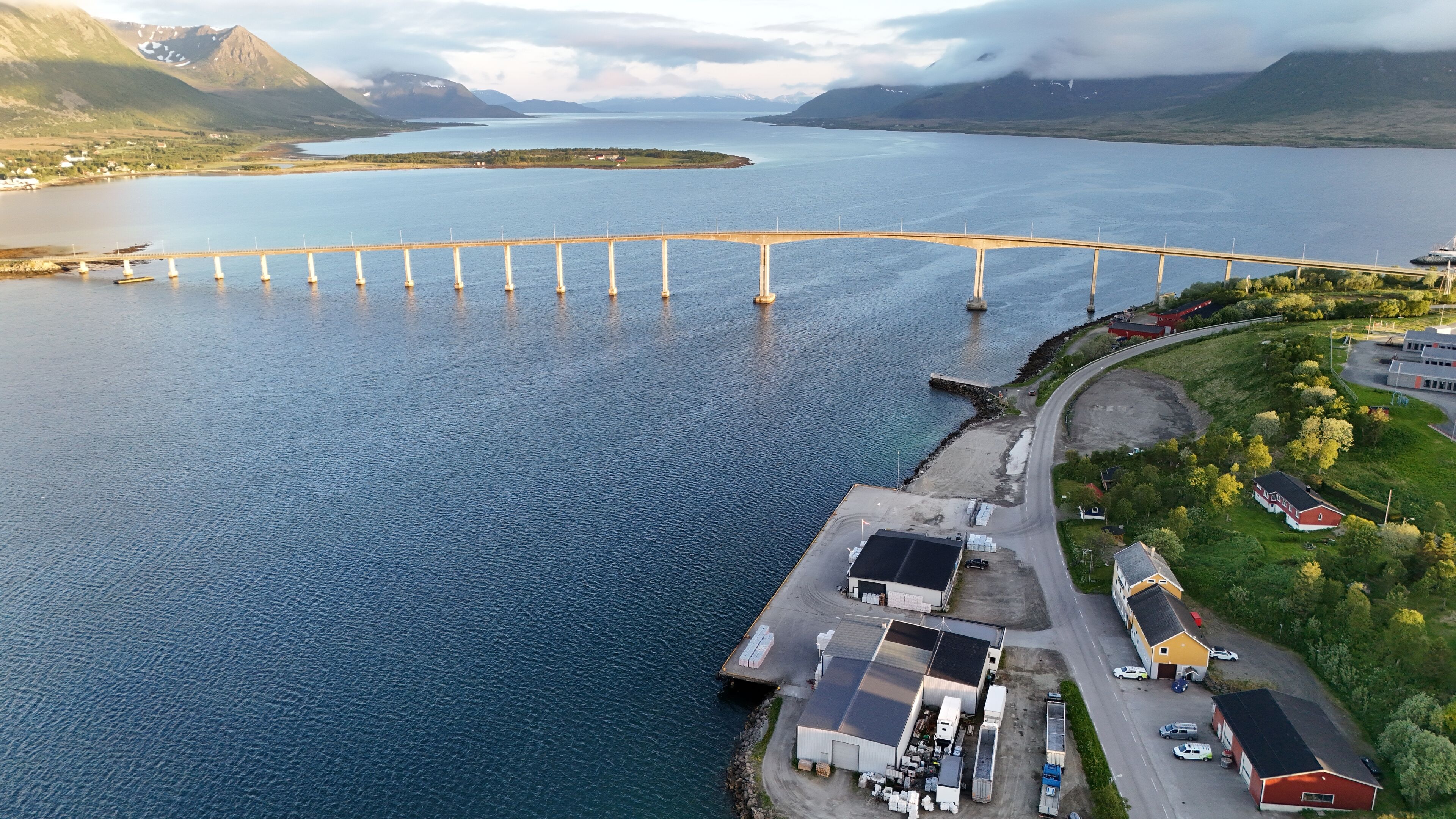An aerial view of a coastal area with a bridge, a dock, and industrial buildings.