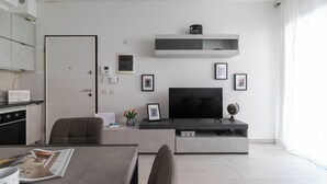 A modern living room with a flat-screen TV, a coffee table, and a dining area with a table and chairs. - Italianway Comfort - Fara 29 (Milan)