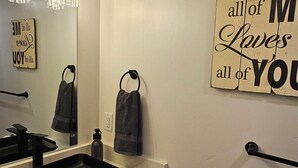 A modern bathroom with a black sink, a mirror, and a towel rack. There are decorative signs on the wall and a towel hanging on the rack. - Gray Haven Near Zion 
& Bryce  (Glendale)