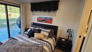 A bedroom with a large bed, a window with curtains, a painting on the wall, and a small bedside table with a clock. - Gray Haven Near Zion 
& Bryce  (Glendale)