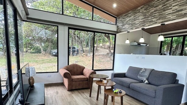 A modern living room with a large window, a grey sofa, a brown armchair, and a small coffee table. - Cabana Vergara Santa Fe (Provincia de Veraguas, Panama)