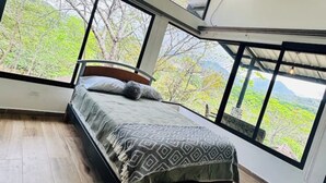 A bedroom with a large bed, a view of trees through large windows, and an air conditioning unit on the wall. - Cabana Vergara Santa Fe (Provincia de Veraguas, Panama)