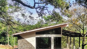 A modern, single-story building with a stone exterior and large windows, surrounded by trees and a grassy area. - Cabana Vergara Santa Fe (Provincia de Veraguas, Panama)