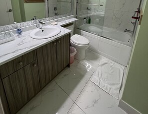 A bathroom with a marble sink, wooden cabinets, a toilet, and a bathtub. - Newton Suite (Surrey)