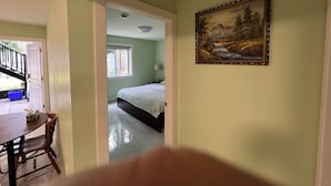 A bedroom with a bed, a window, a painting, and a staircase leading to another room. - Newton Suite (Surrey)