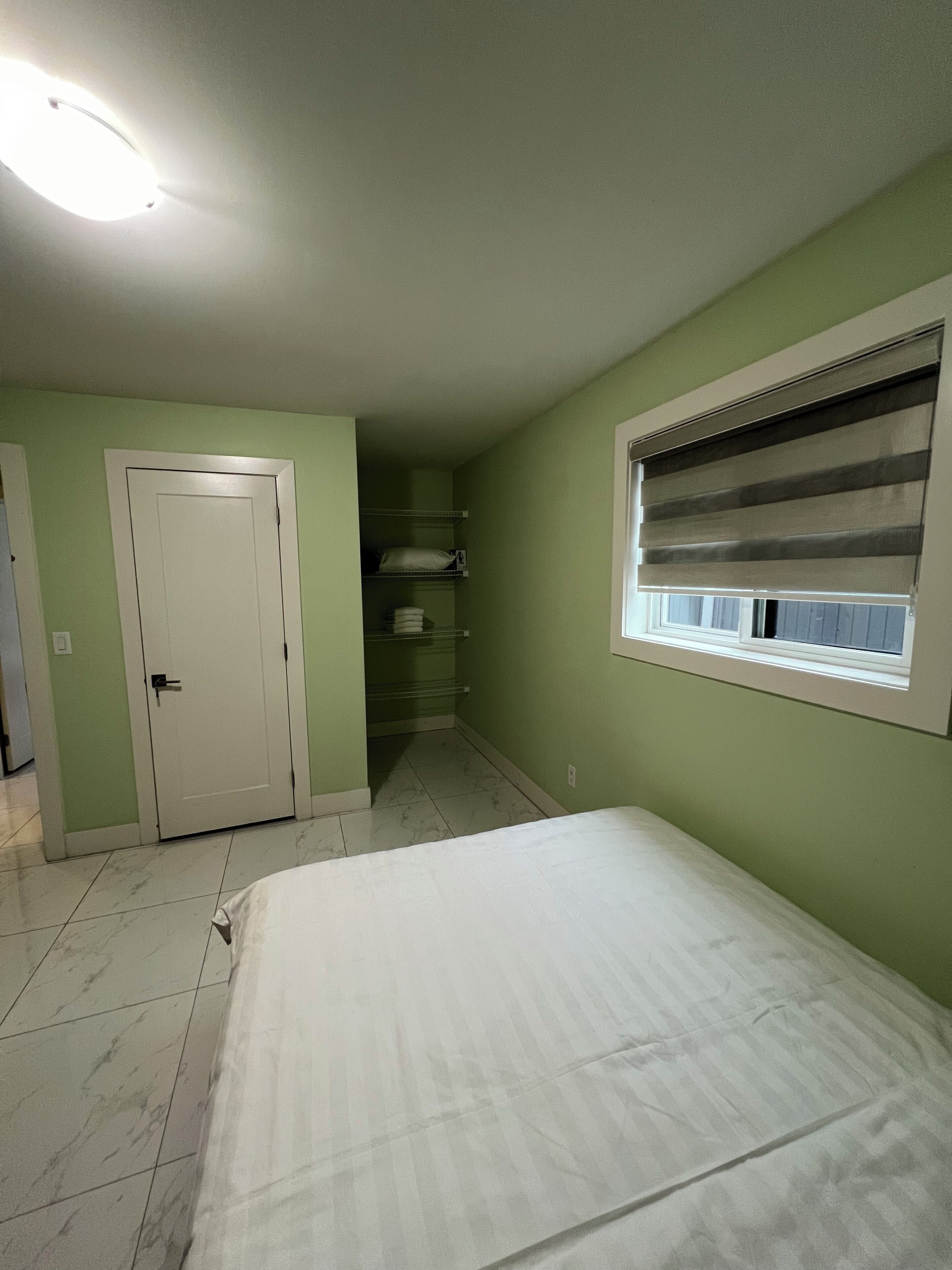 Un dormitorio con cama, armario, ventana con persianas y puerta.