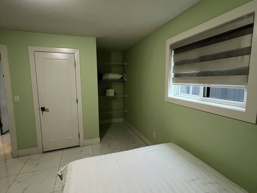 Een slaapkamer met een bed, een kast, een raam met jaloezieën en een deur.