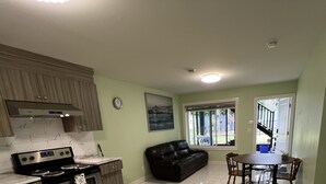 A compact kitchen with a stove, oven, and cabinets, a black leather couch, and a dining table with chairs. - Newton Suite (Surrey)