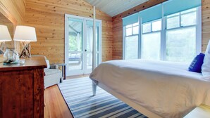 A wooden-paneled bedroom with a large bed, a nightstand, and a window with blinds.