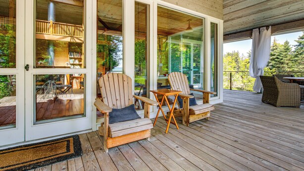 A wooden deck with two Adirondack chairs and a small table, overlooking a lush green landscape.