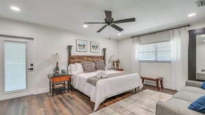 Et soveværelse med seng, sengeborde, loftventilator og et vindue med persienner.