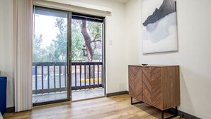 Une pièce dotée d’une porte-fenêtre coulissante donnant sur un espace extérieur, d’un meuble en bois et d’une œuvre d’art encadrée accrochée au mur.