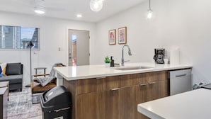 A modern kitchen with a central island, a built-in dishwasher, and a window with blinds. - Immaculate Apartment in Austin 5 Min to Downtown ATX (Austin)