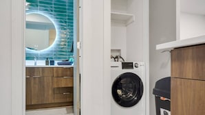 A laundry room with a washing machine, a trash bin, and wooden cabinets. - Immaculate Apartment in Austin 5 Min to Downtown ATX (Austin)