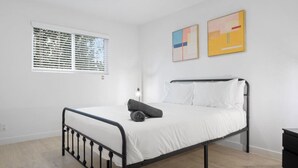 Un dormitorio con una cama, una ventana con persianas y dos cuadros abstractos en la pared.