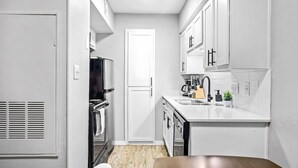 Una cocina compacta con armarios blancos, horno empotrado y lavabo.