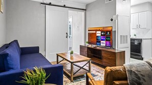 Una sala de estar moderna con un sofá azul, una mesa de centro de madera y un televisor mostrando servicios de transmisión.